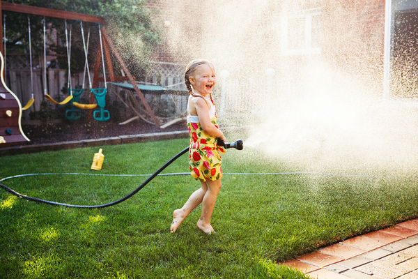 Little girl with a hose spaying water on the lawn