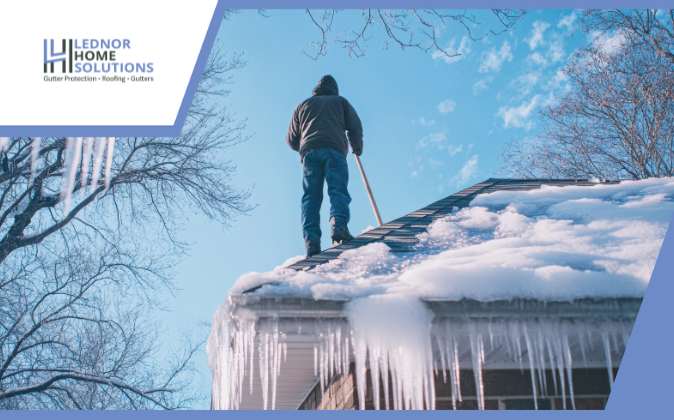 person on a house rooftop clearing the ice in winter