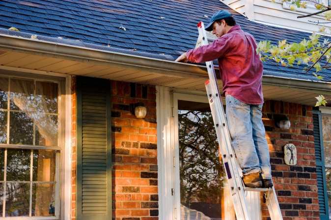 man on a ladder cleaning gutters during spring