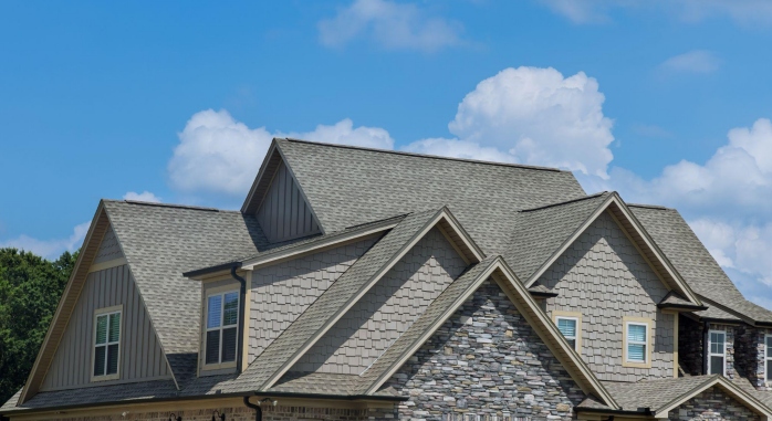 Complex shingled roof on house under blue sky.