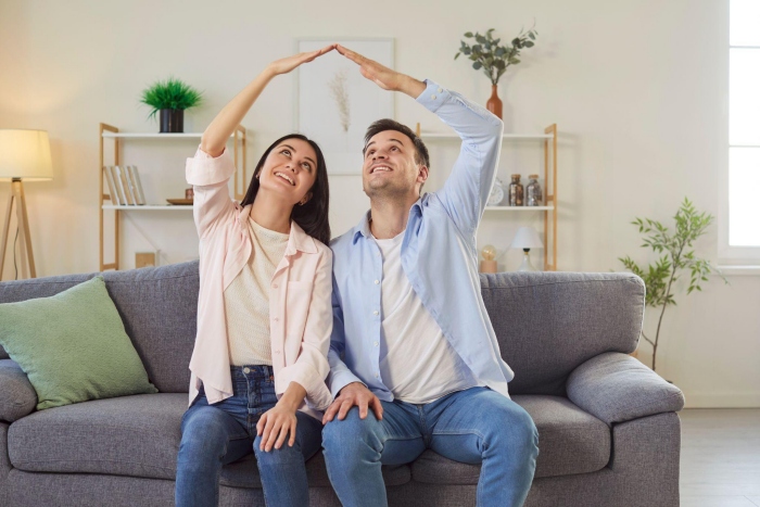 Couple forming house roof with hands on couch.